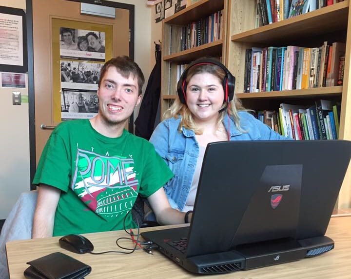 two students smiling sitting at a desk with a lap top working together in a university study space.