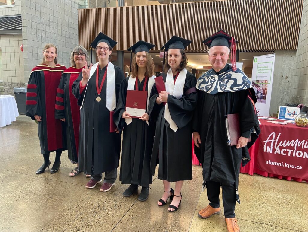 Three graduates in graduation robes and hats standing with President Davis, Dr. Fiona, and Dr Jennifer, all in graduation regalia.