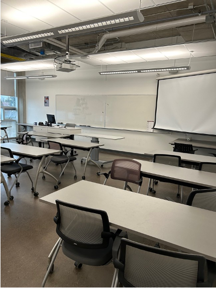 Image of classroom 3830, rows of two seater tables and chairs, white board and screen at the front